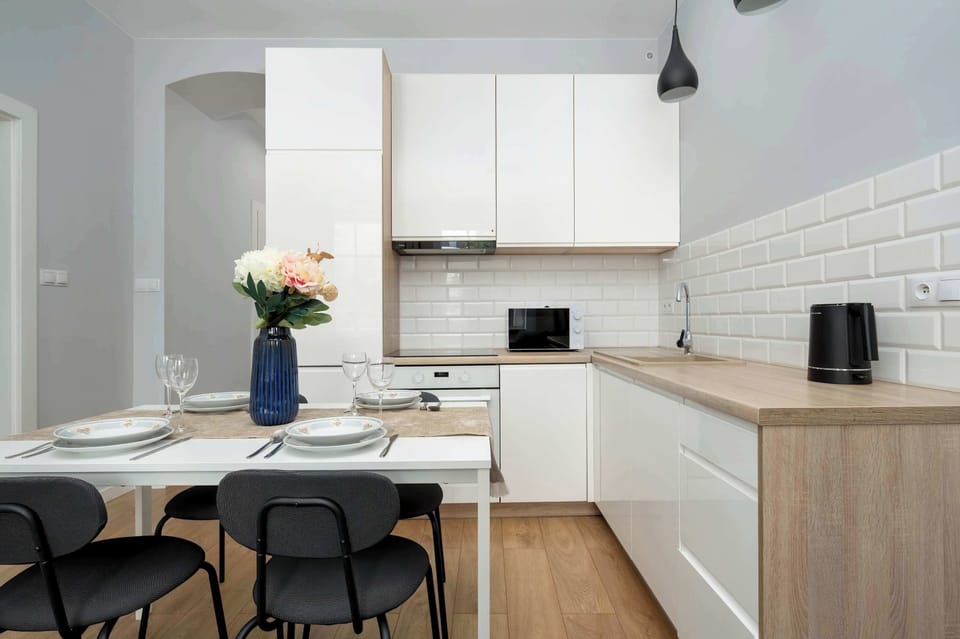 A modern dining space with a table set for four, adjacent to a white kitchenette with upper and lower cabinets.