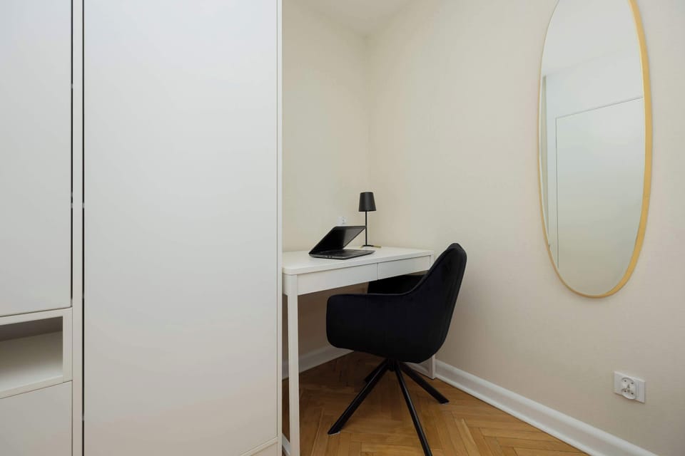 A small home office corner with a desk, chair, and mirror on the wall.