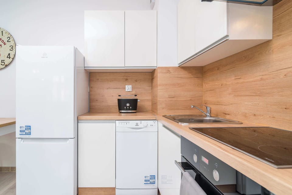 A compact kitchen with white cabinets and wooden backsplash. There's a fridge, microwave, and an electric stove.