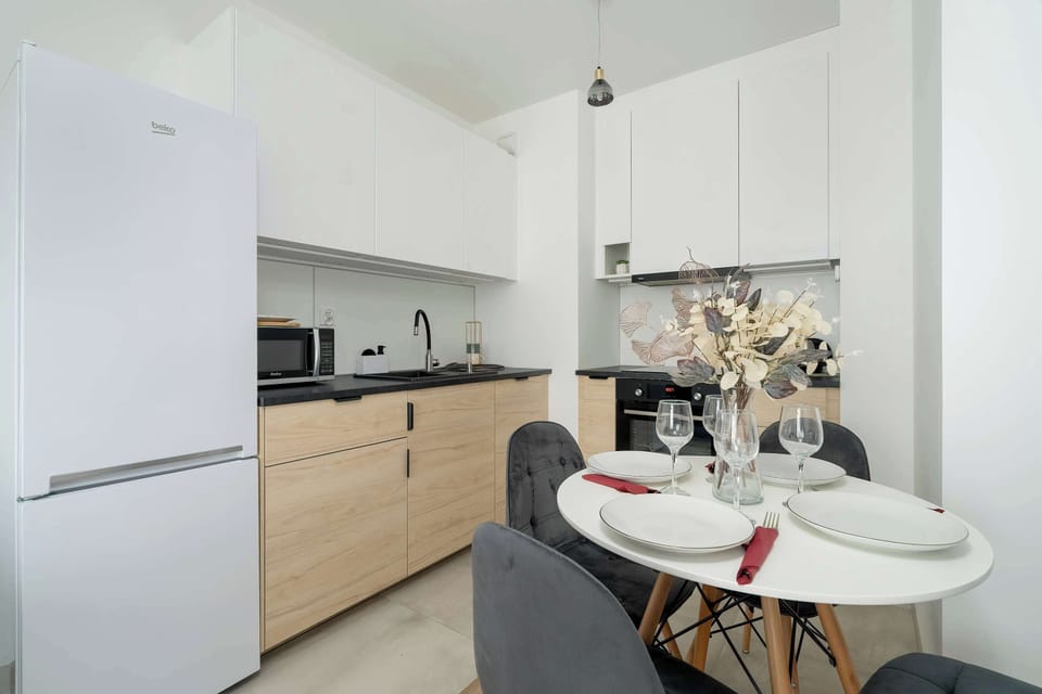 A compact, modern kitchenette with white cabinetry and a small round dining table set with elegant decor.