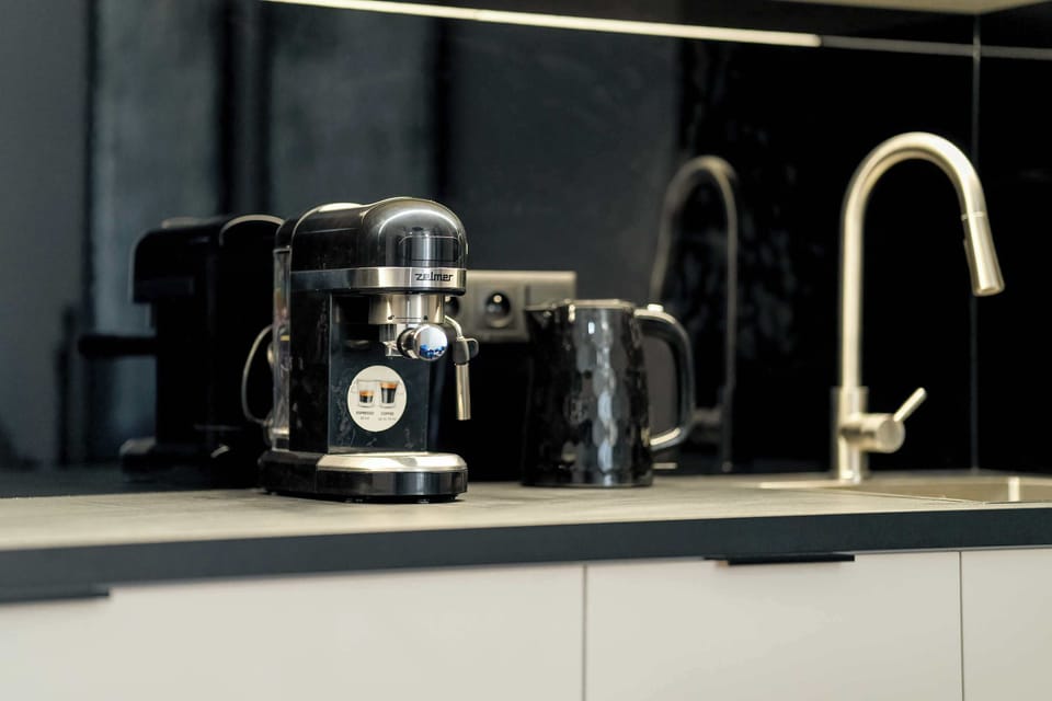 Another view of the kitchen showcasing a sleek coffee machine on the bright countertop. The black backsplash makes the space appear larger, and the bold cabinets contrast with the bright walls.
