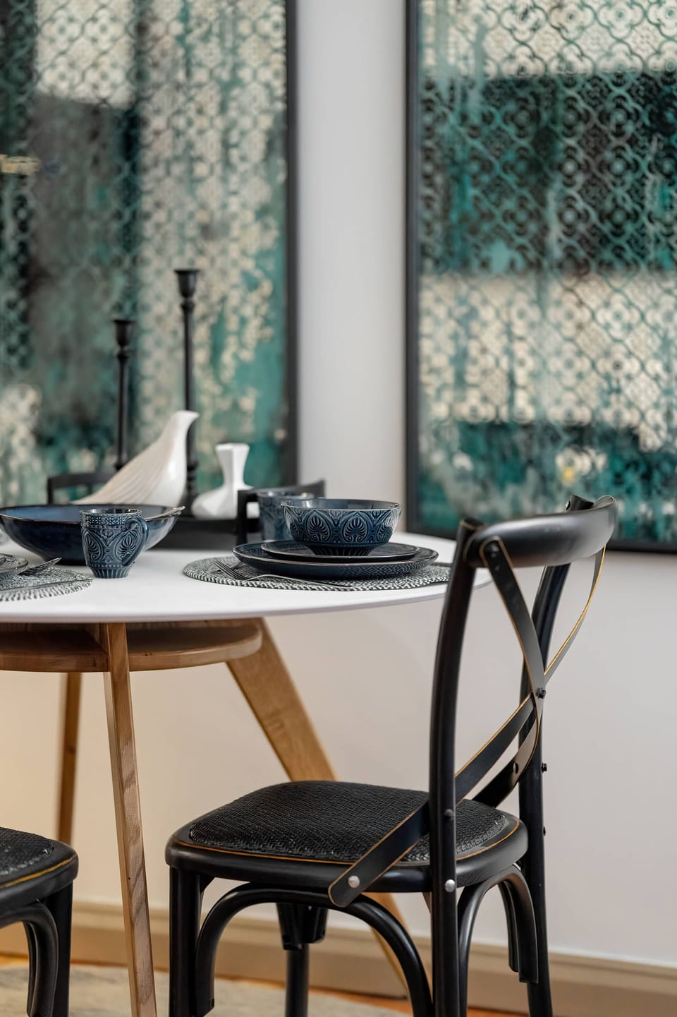 Dining table with round top wooden legs. Next to the table are chairs, There are decorative mirror panels on the wall.