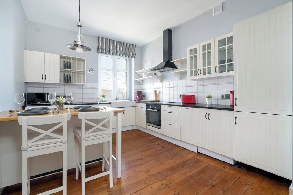 A long kitchen with white cabinetry and wooden countertops, featuring a dining table with chairs set up for a meal.