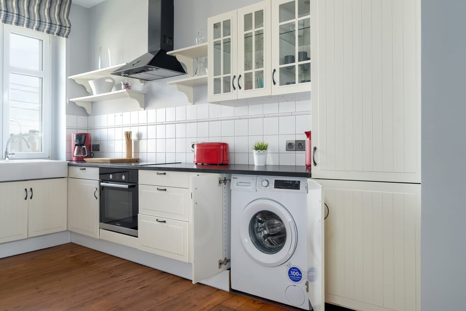 A view of the kitchen workspace with a built-in stove, oven, and washing machine under sleek white cabinets and open shelving.