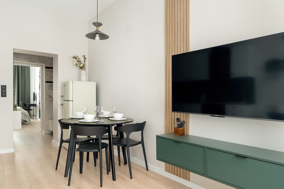 A modern living room with a mounted TV, dining area, and neutral tones. Clean lines and ample lighting enhance the room’s functionality.