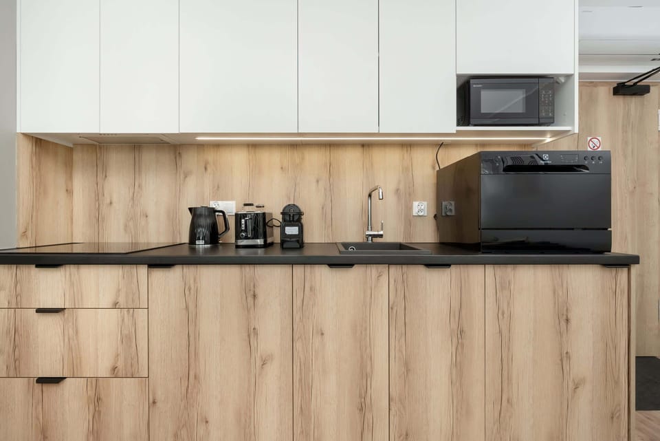 A minimalist kitchenette with woodgrain lower cabinets, a stovetop, microwave, and compact storage space.