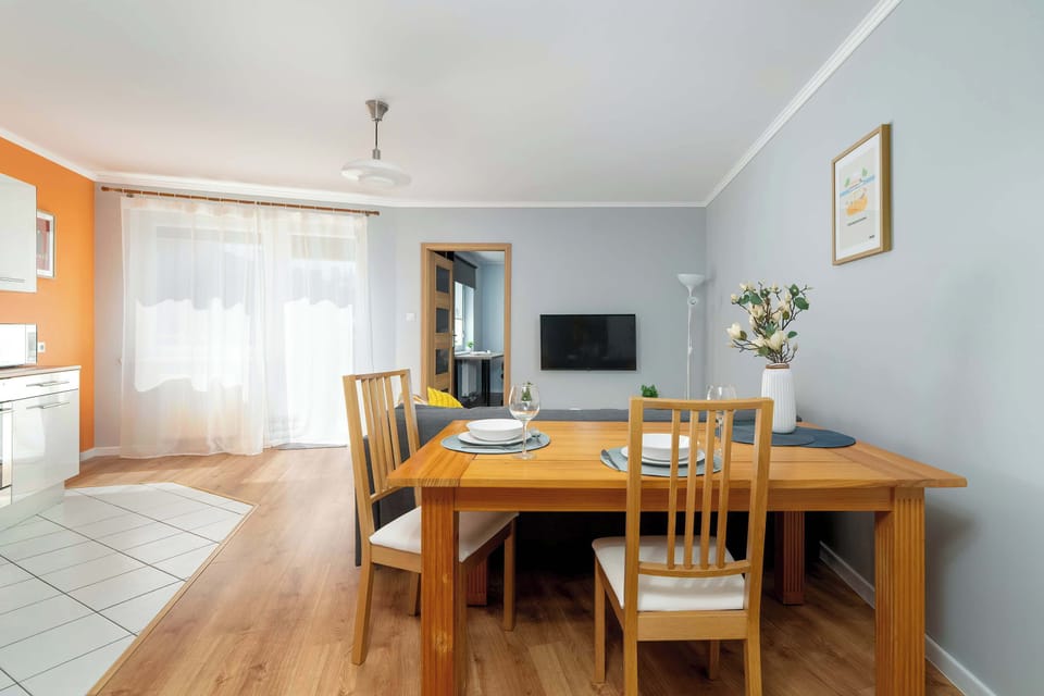 A wider angle of the living and dining space, including a wooden dining table, sofa, and large window for natural light.
