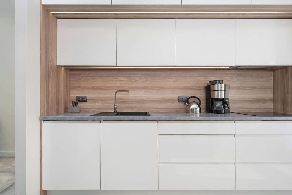 The kitchen is modern and neat, with white cabinets, wooden accents and modern appliances, such as an oven, induction hob and refrigerator.