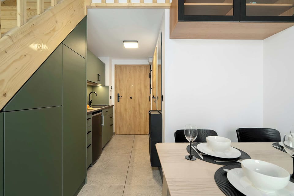 An elegantly furnished living room with a kitchenette, a round table with four chairs, and modern ceiling lighting creates a pleasant space for relaxation and dining.