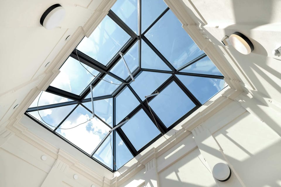 A modern skylight atrium with white beams and glass panels, creating a bright architectural feature in the stairwell.

