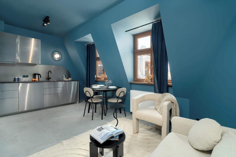 A sloped-ceiling room with a small dining nook, plush seating, and ample natural light coming through traditional windows.

