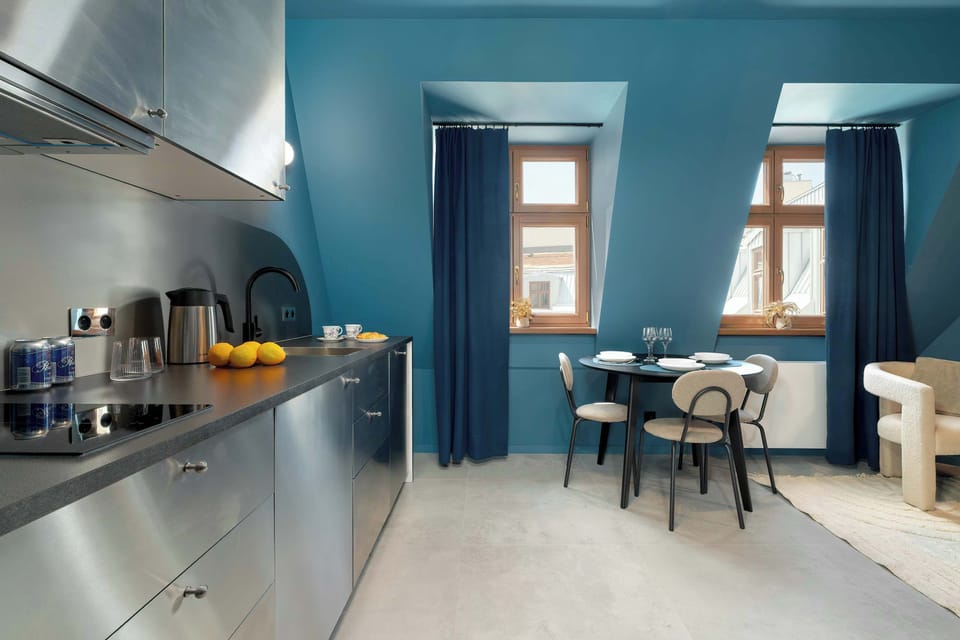 A contemporary open-plan space with a built-in kitchen, soft seating, and a sculptural mirror mounted on the blue wall.