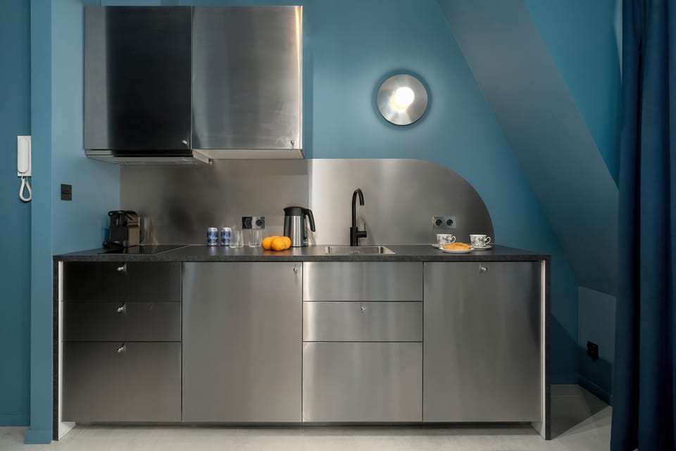 A modern kitchenette with sleek stainless steel cabinetry, open shelving, and under-cabinet lighting.

