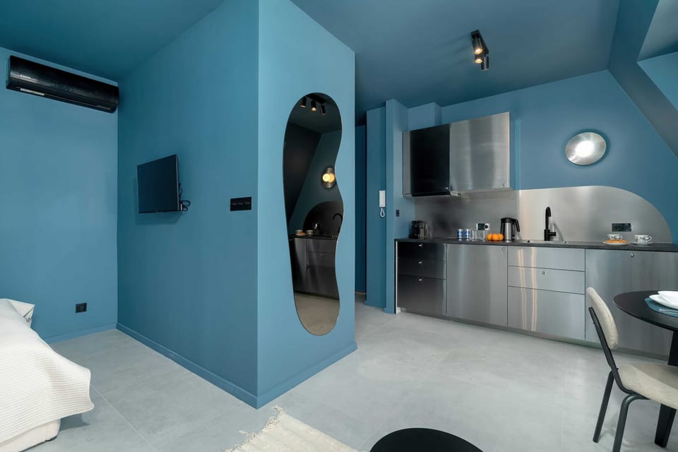 A bright blue attic-style living room combining a kitchen, lounge area, and window seating with coordinated decor.
