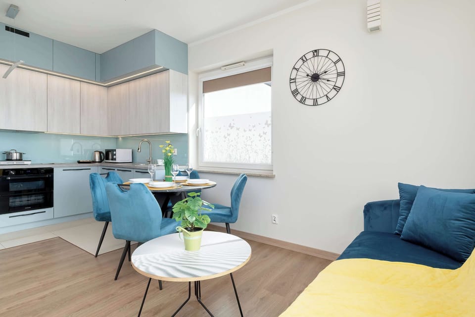 A bright living area with a blue sofa, yellow throw, and a large clock on the wall.