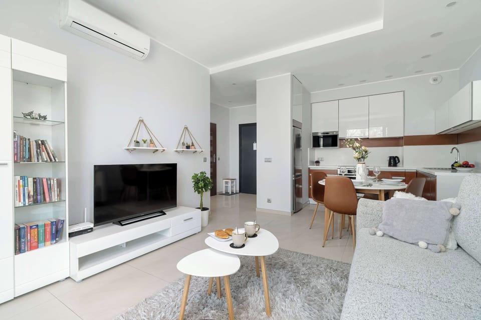 An air-conditioned living room with a large window providing plenty of natural light, a sofa bed for relaxing and a Smart TV.
