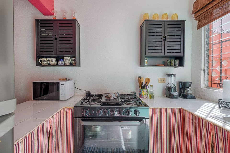 This gorgeous kitchen offers everything needed for preparing meals, including a four-burner gas range, microwave, and coffee maker. The ample white tile counters and charming striped curtain create a bright, functional, and intimate cooking space.