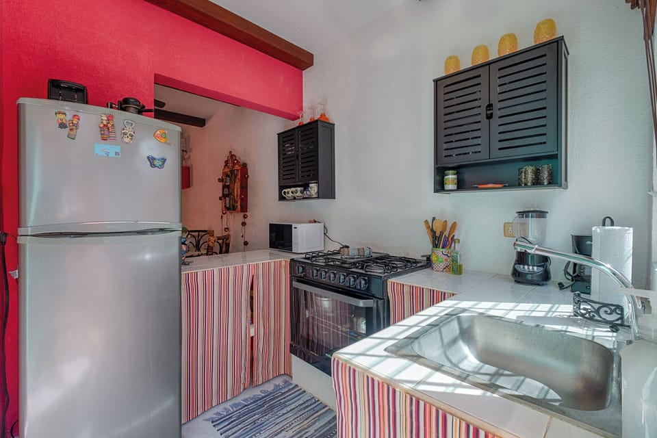 Prepare meals in this uniquely styled kitchen! Featuring a silver refrigerator and a full gas range, the space pops with a striking red accent wall and charming striped curtain details, creating a bright, intimate, and fully functional cooking space.