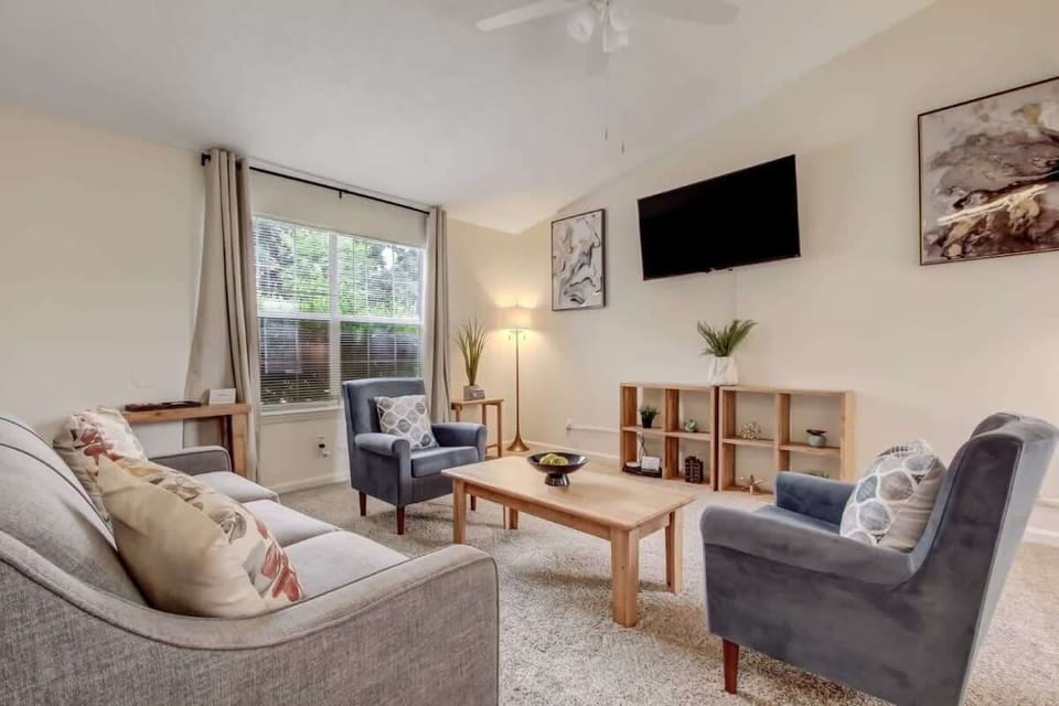 The living room offers a relaxing space with seating, flat-screen TV, and plenty of natural light.