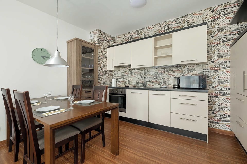 A compact kitchen with a workspace and dining area, featuring light cabinetry and wallpapered walls.

