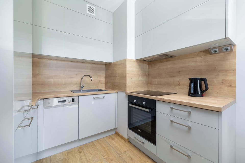 A compact, modern kitchen with sleek, white cabinetry and a wooden countertop. The kitchen is fully equipped with an oven, stove, and sink, all designed with minimalist style in mind.