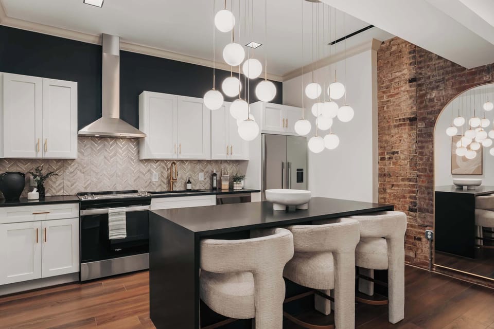 The modern kitchen boasts a central island with plush barstools, illuminated by a playful chandelier that adds character to the space.