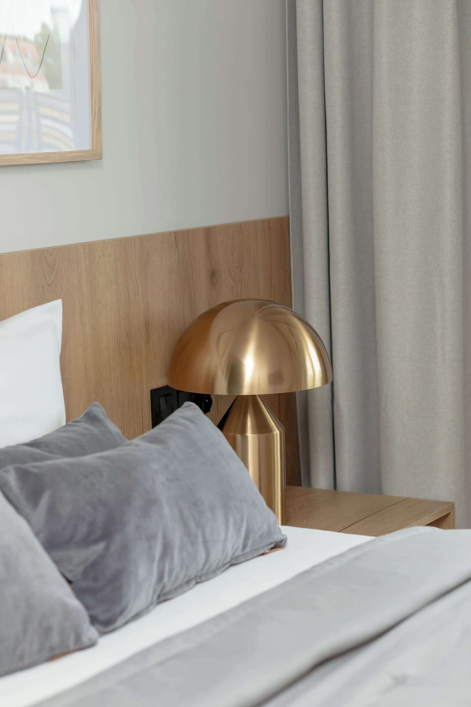 A partial close-up of a neatly made bed and a golden lamp on a small wooden nightstand.