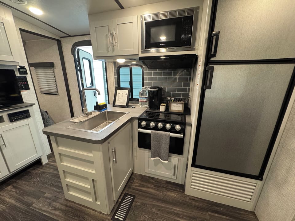Fully equipped kitchen with fridge, microwave, stove, and Keurig machine.