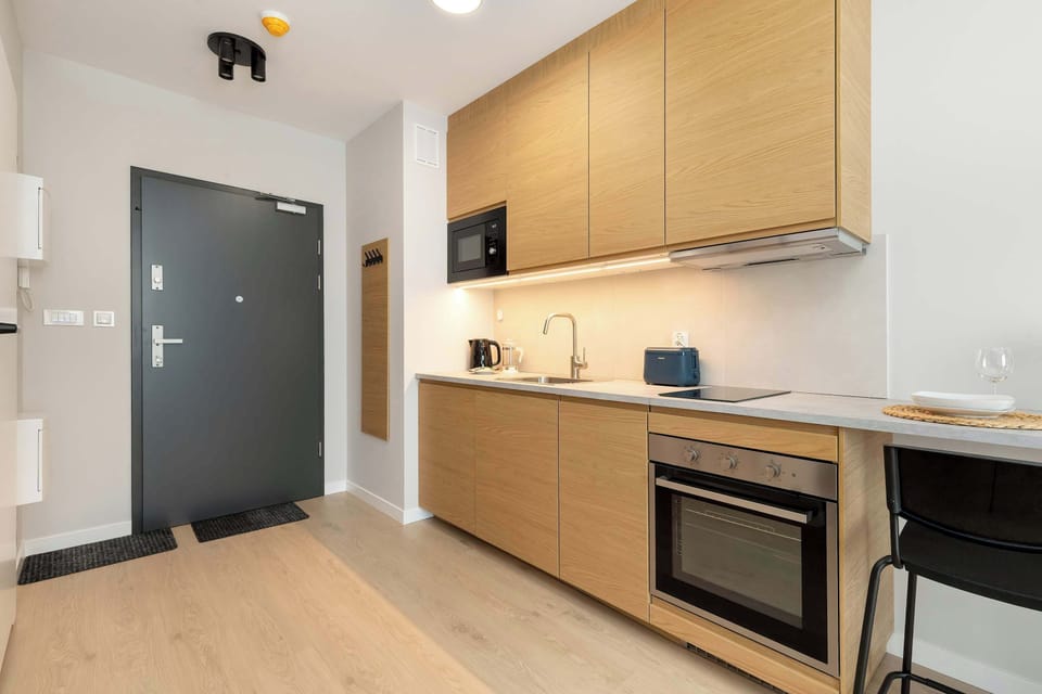 A view of a kitchen and hallway area with a black door, light cabinetry, and modern lighting.