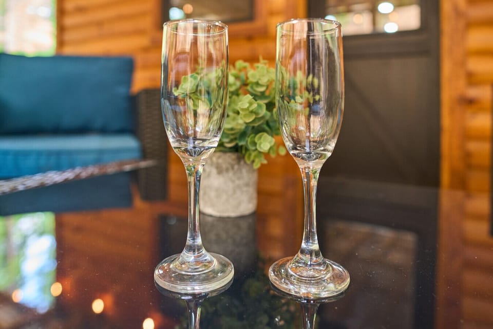 Close-Up of Two Champagne Glasses | Reflections on Glass Table with Cozy Cabin Background