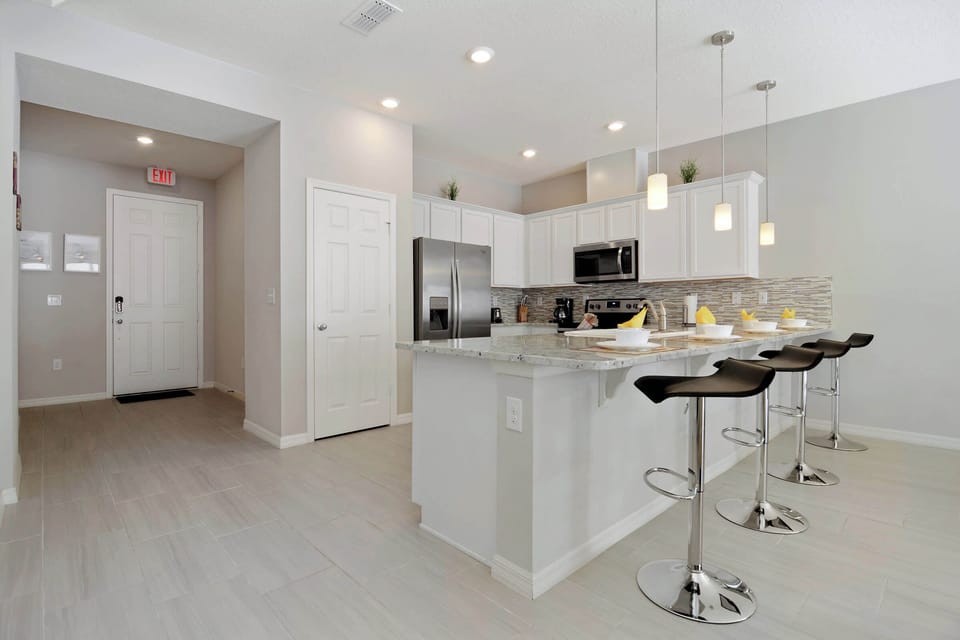 Contemporary breakfast bar invites casual bites-sleek pendants, chrome stools, and airy neutrals create a clean, modern vibe before a day of fun.