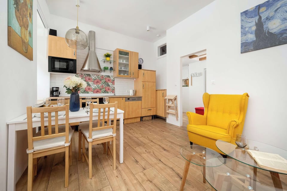 A dining table for four with wooden chairs and kitchen storage in the background.