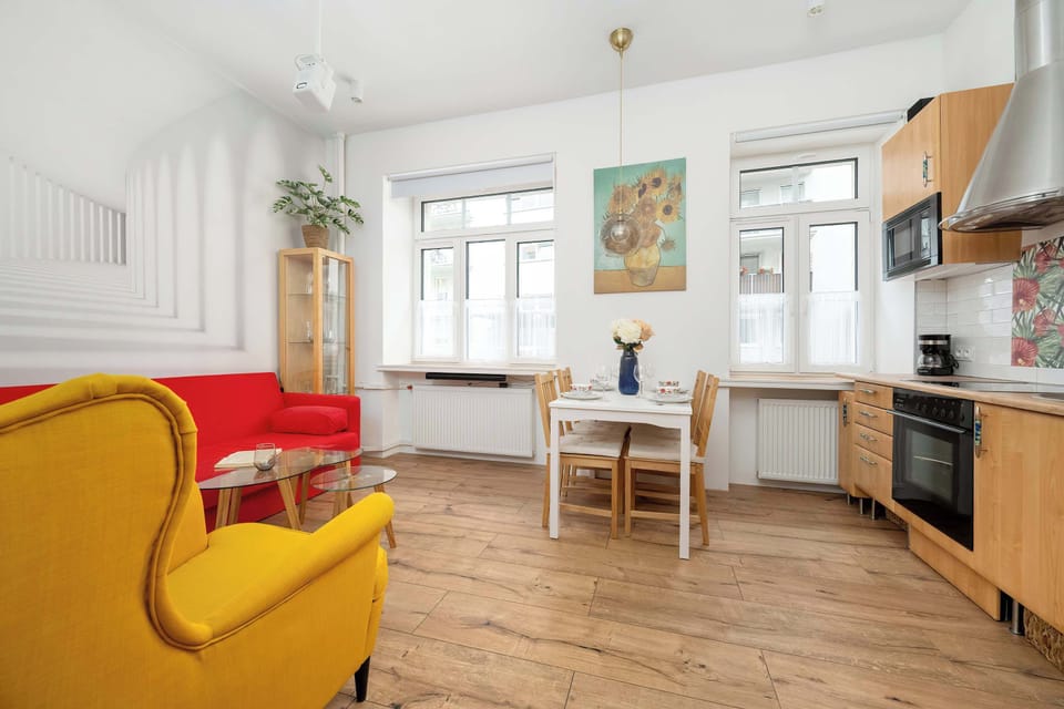 A view of the living and kitchen space with natural light from the windows and bright furniture.