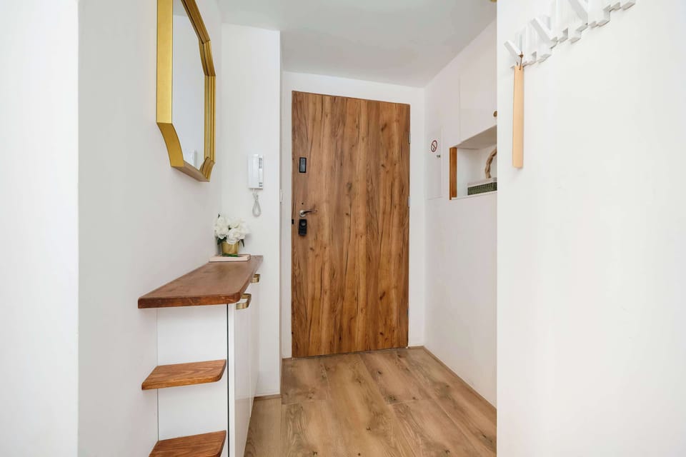 A hallway with white walls, wooden flooring, a gold-framed mirror, and decorative accents.