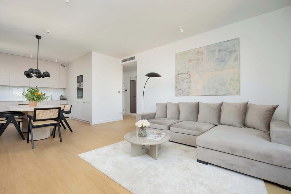 A spacious living room with a corner sectional and large artwork. A soft rug and wooden floors enhance the cozy feel.