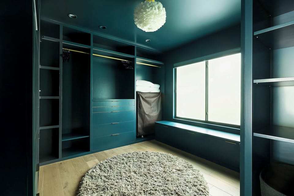 A stunning walk-in closet with bold navy walls, custom shelving, and a glam overhead light—ideal for extended stays.