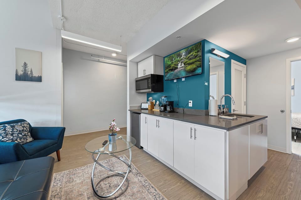 Cozy unit with stylish kitchenette, coffee setup, TV, & vibrant accent wall.
