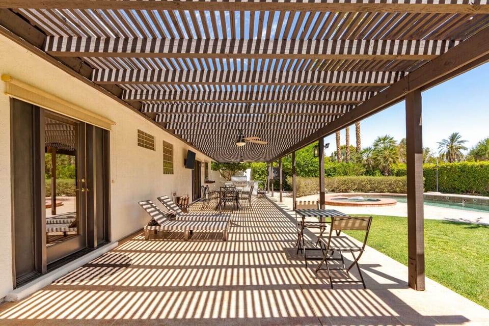 Covered patio w/ long dining table & shade overhead, perfect for relaxed outdoor meals any time of day.