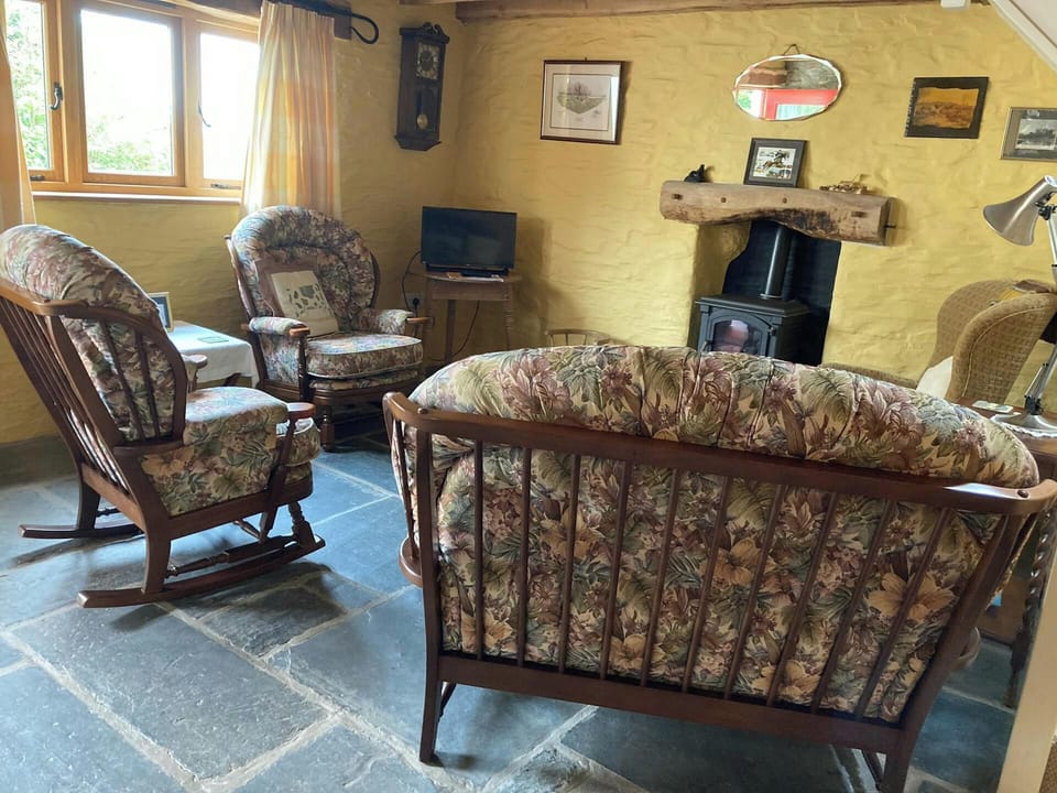 Sofa, armchairs, small table with lamp, TV on table, wood burner and slate floors