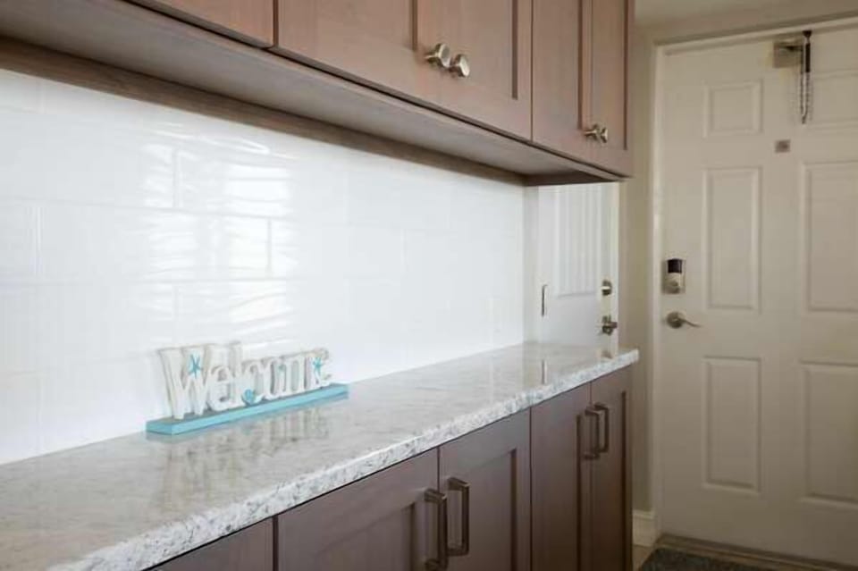 Step into your coastal getaway with a bright, welcoming entryway featuring granite counters and a charming “Welcome” sign—setting the tone for a relaxing beach vacation.