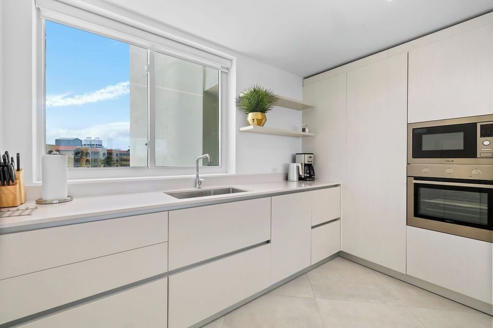 Bright kitchen with sleek cream cabinetry and stainless appliances ready for your culinary adventures. City views through the window add a refreshing touch.