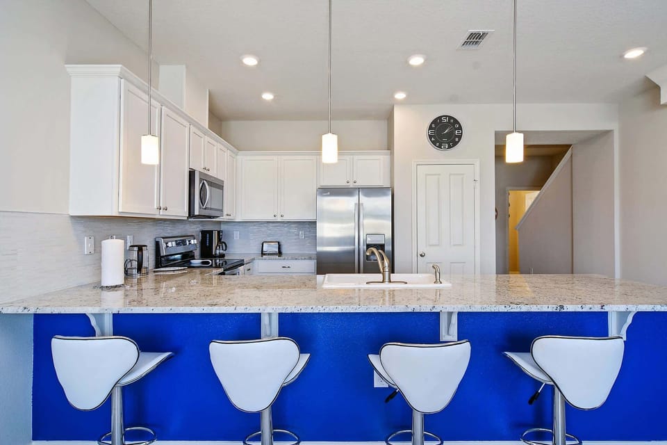 Start your day at this bright breakfast bar, featuring four comfy stools, chic lighting, and a modern kitchen perfect for any group gathering.