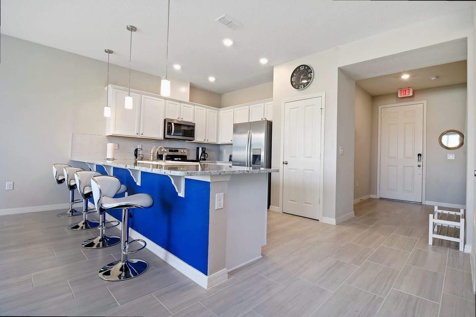 Pull up a seat at the vibrant breakfast bar in this modern kitchen, featuring stylish pendant lights and a bold blue accent for a welcoming touch.