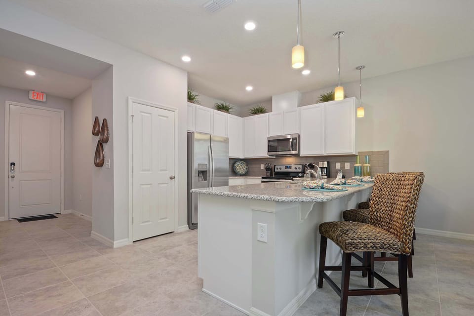 Bright, modern kitchen with white cabinets, stainless appliances, and a granite island-coastal touches and pendant lights make cooking here a joy.