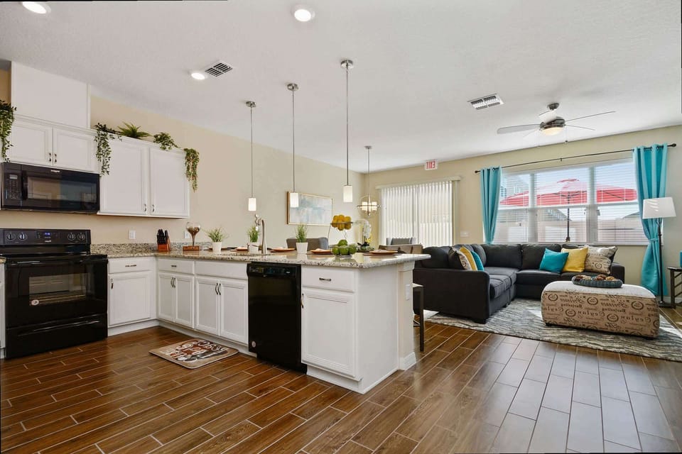 Cook & connect in this open kitchen lined with white cabinets, granite island & sleek black appliances opening to the cozy living area.