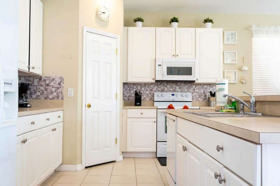 Bright and tidy kitchen with white cabinets, a mosaic backsplash, and a cozy breakfast bar. Perfect for preparing meals and enjoying casual dining!