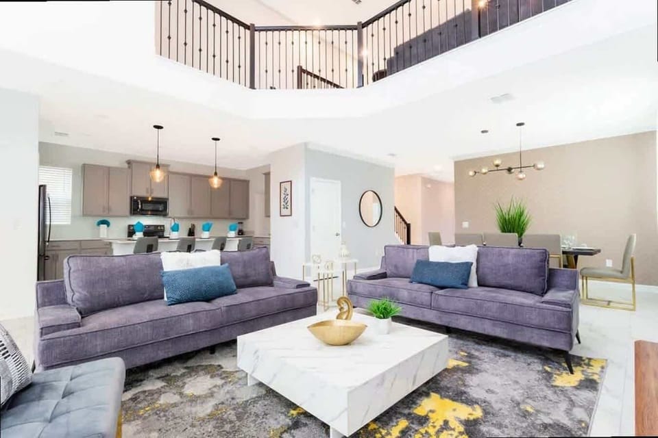 Lounge in comfort in this vibrant open living area with modern decor, cozy purple sofas, and bright natural light-ideal for unwinding with loved ones.