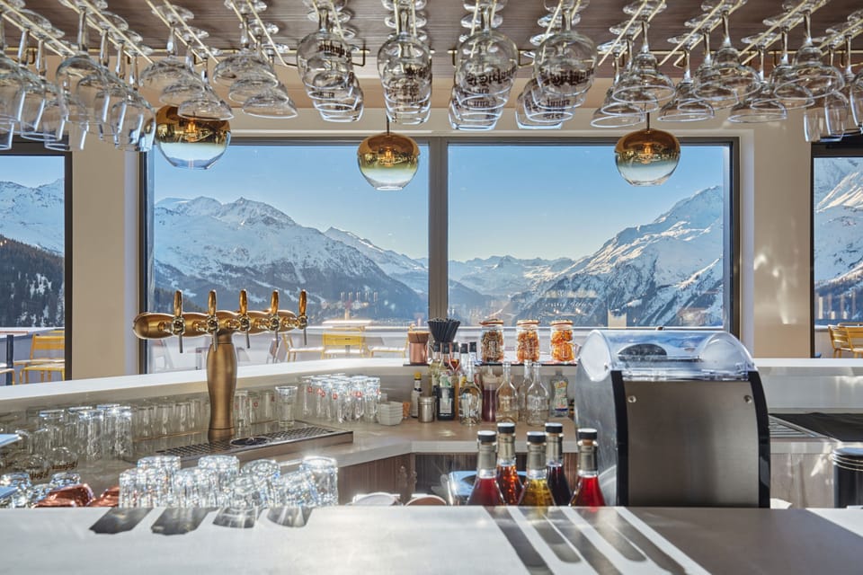 Bar area with beer taps and glassware set against a large window framing the snow-capped peaks outside.