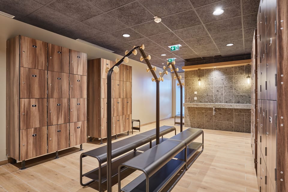 Locker room with numbered wooden lockers, black metal benches, and stone-finish walls adjacent to the wellness area.