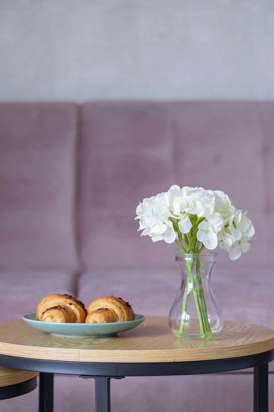 A tray with a flower vase and pastries placed on a dark side table.

